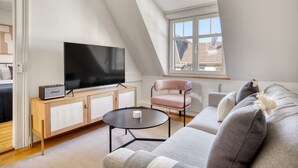 A modern living room with a television, a sofa, a chair, and a small table. - Charming Breite 3 Room w/ Washer & Storage, nr Market, by Blueground (Basel)