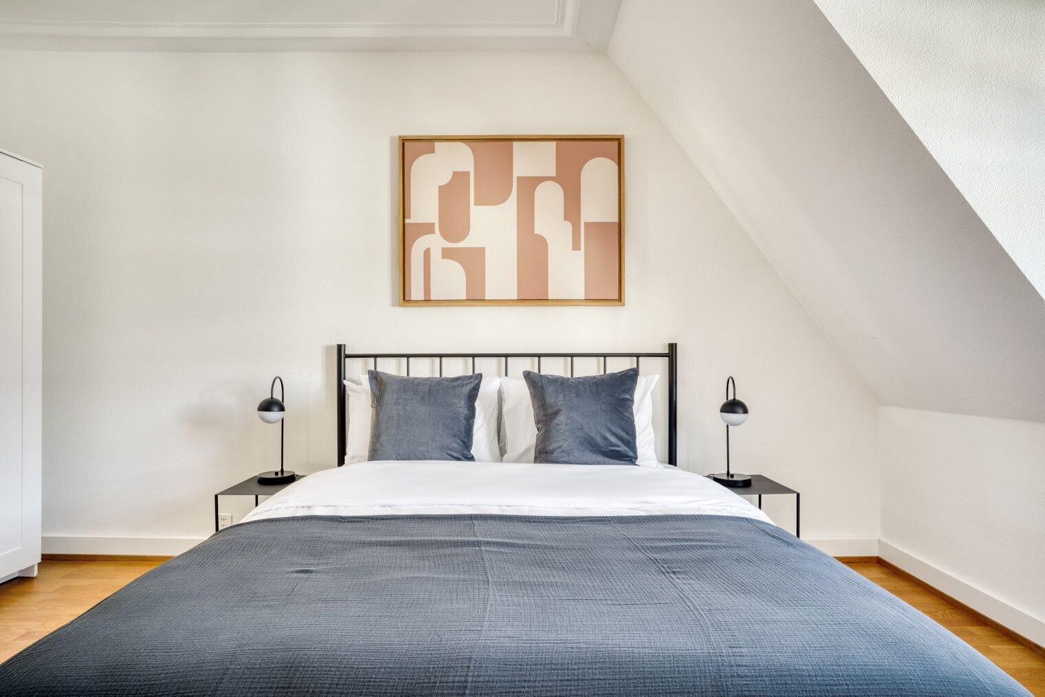 A bedroom with a large bed, a modern headboard, two bedside tables, and a wall-mounted abstract artwork.