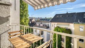 A balcony with a wooden table and chairs, overlooking a residential area with houses and a construction site. - Charming Breite 3 Room w/ Washer & Storage, nr Market, by Blueground (Basel)