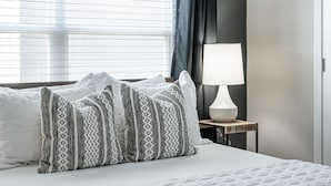 A neatly made bed with patterned pillows, a bedside lamp, and a window with blinds.