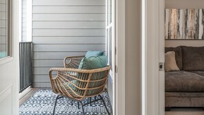 A room with a wicker chair, a patterned rug, a gray sofa, and a piece of abstract art on the wall.