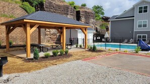 A covered picnic area with benches and a pool in the background.