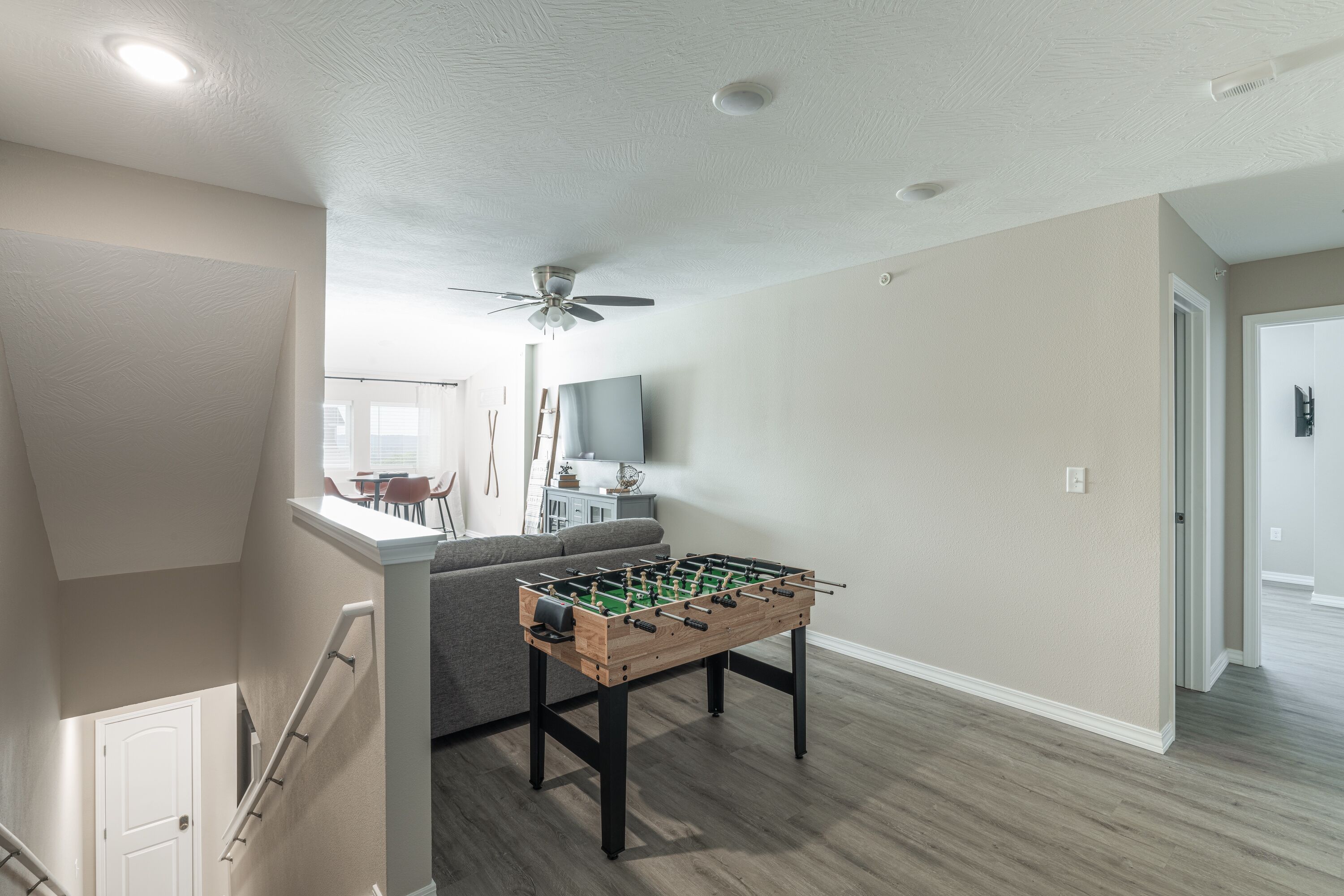 A spacious living area with a foosball table, a ceiling fan, and a staircase leading to another level.