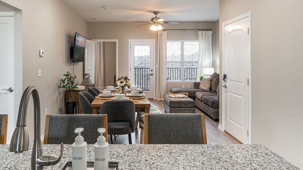 A modern kitchen with granite countertops, a dining area with a table and chairs, a built-in oven, and a ceiling fan.