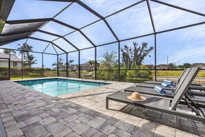 A covered outdoor swimming pool with lounge chairs and a hat on one of them. - Close to Golf, Fishing in the Canal, Heated Saltwater Pool, - Villa Cloud 9 - Roelens Vacations (Cape Coral)