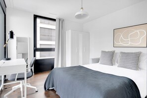 A modern bedroom with a large bed, a desk, and a wardrobe.