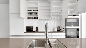 A modern kitchen with white cabinetry, a stainless steel sink, and built-in appliances including a microwave, toaster, and oven. - Luxe Opfikon 4.5 Room w/ Storage & W/D, 2 mins to Market, by Blueground (Zurich)