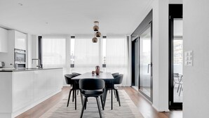 A modern kitchen with white cabinets, a dining area with a black table and chairs, and a large window providing natural light. - Luxe Opfikon 4.5 Room w/ Storage & W/D, 2 mins to Market, by Blueground (Zurich)