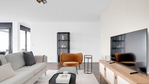 A modern living room with a sofa, ottoman, coffee table, and a television on a wooden cabinet. - Luxe Opfikon 4.5 Room w/ Storage & W/D, 2 mins to Market, by Blueground (Zurich)