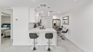 Una cocina moderna con armarios blancos, una isla central con taburetes y un cartel que dice 