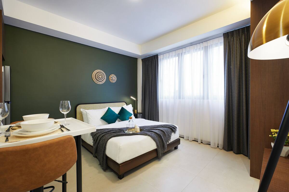 A hotel room with a bed, bedside table, and a dining area with a table set for two.