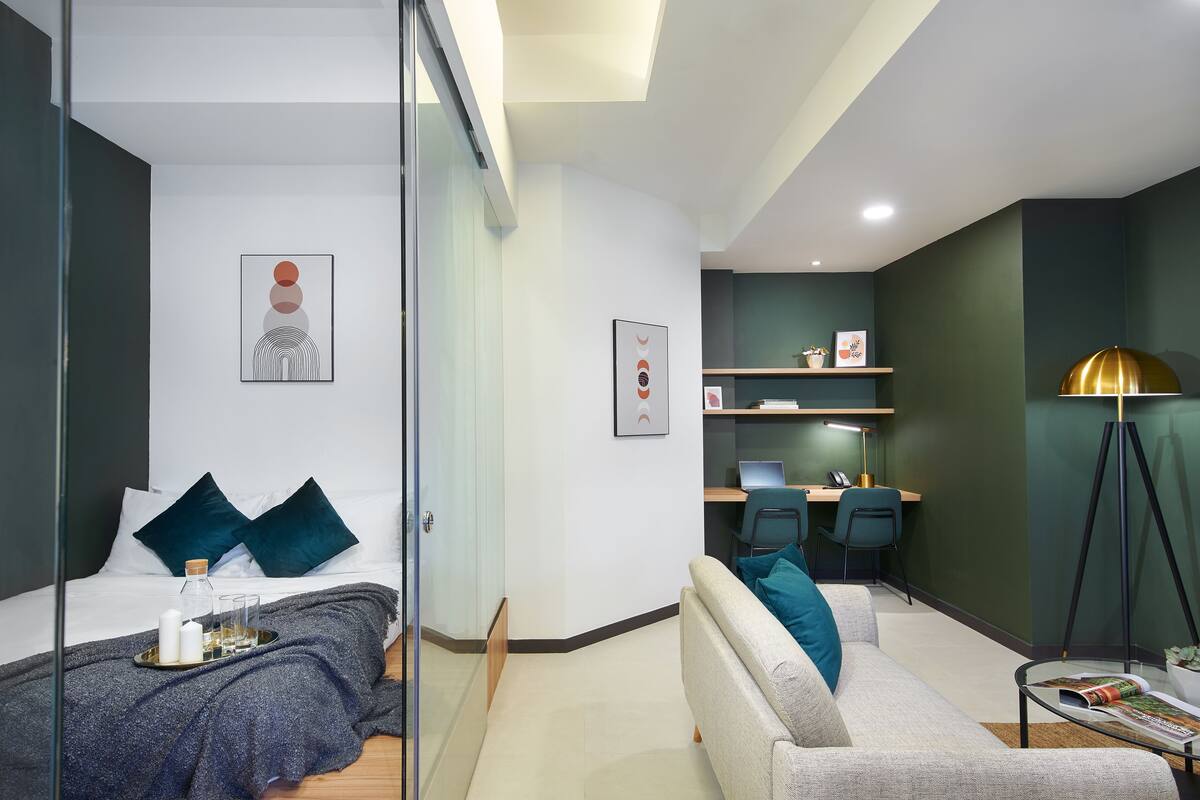A modern hotel room with a bed, bedside table, and a desk area with a computer and chair.