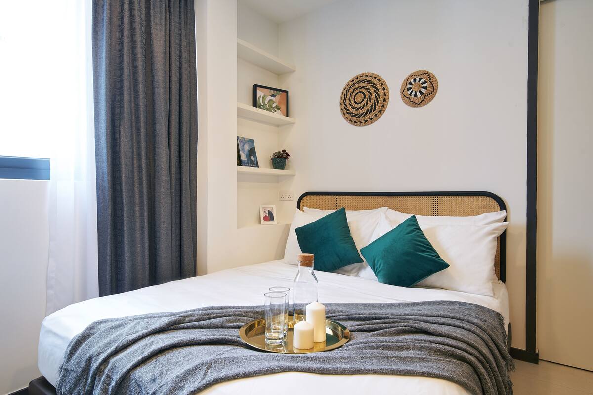 A neatly made bed with a tray of candles and glasses, a wicker headboard, and decorative wall art.
