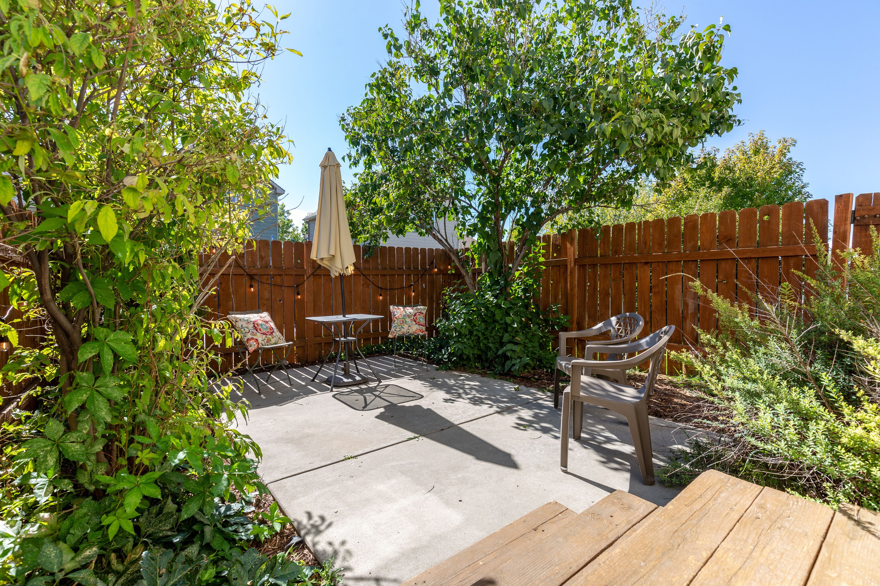 A backyard patio with a wooden deck, two metal chairs, a small round table, and a beige umbrella.