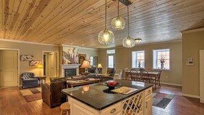 Un vaste espace de vie doté d’un plafond en bois, d’un îlot central avec un plan de travail noir et d’un coin repas comprenant une table et des chaises en bois.