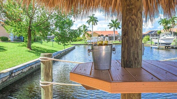 Una terraza de madera con un cubo de metal que contiene botellas, una cuerda y un techo de paja.