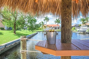 A wooden deck with a metal bucket holding bottles, a rope, and a thatched roof overhead. - Sweet Retreat - Near to the Caloosahatchee River (Cape Coral)