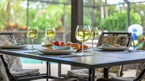 Una mesa de comedor con tres copas de vino, platos con comida y vistas a la vegetación a través de un cerramiento de vidrio.
