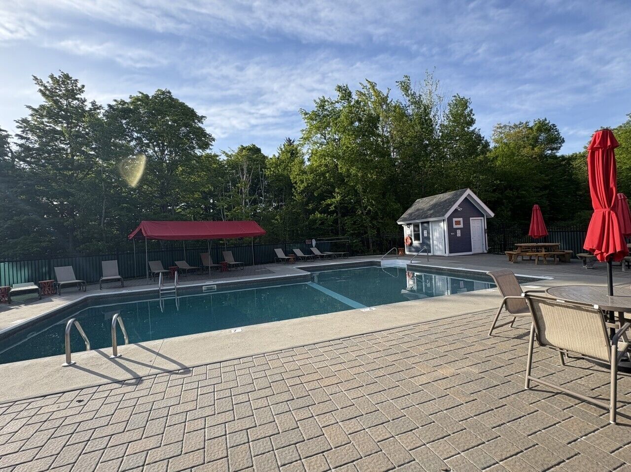 A swimming pool with lounge chairs and a small building, surrounded by trees.