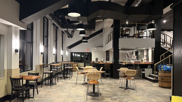 Un restaurante espacioso con techos altos, conductos a la vista y una combinación de mobiliario de madera y metal.