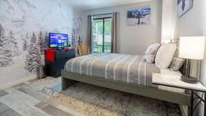 Un dormitorio con cama, escritorio, televisor, ventilador de techo y ventana con cortinas.