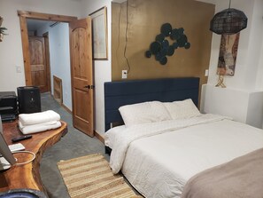 Une chambre à coucher avec un lit, un bureau en bois avec un ordinateur, une télécommande et un haut-parleur.