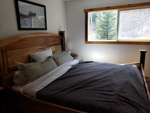 Una cama con cabecera de madera, una ventana con vista a árboles y un cuadro en la pared.