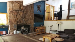 A room with a stone fireplace, a television mounted on the wall, a sofa, a coffee table, and a small round table.