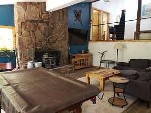 A room with a stone fireplace, a television mounted on the wall, a sofa, a coffee table, and a small round table.