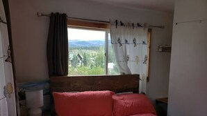 A bedroom with a wooden headboard, a bed with pink bedding, a window with curtains, and a view of a forested area.