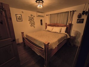 A bedroom with a wooden bed, a nightstand, a wall-mounted air conditioner, and a ceiling light fixture.