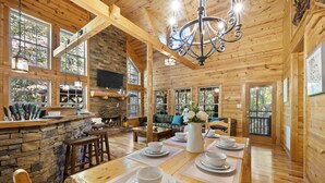 Un intérieur en bois avec une table à manger pour quatre personnes, des murs en pierre et de grandes fenêtres.