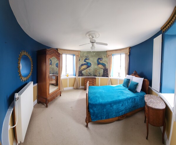 Un dormitorio con cama, cómoda, espejo, ventilador de techo y ventana con cortinas.