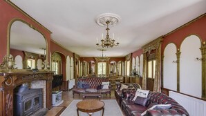 A grand room with a fireplace, ornate mirrors, a chandelier, and plush seating.