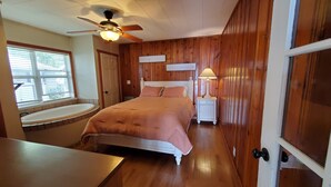 Une chambre à coucher comprenant un lit, une table de chevet, une lampe, un ventilateur de plafond, une fenêtre et une baignoire.