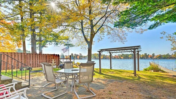 Une terrasse extérieure avec une table et des chaises, une pergola et une vue sur un lac.