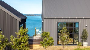 A modern building with a large window and a view of the sea. - Loft & Workroom, Woodside Bay | Be My Guest (Auckland)