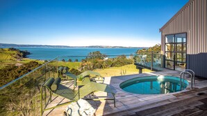 A modern outdoor pool area with a clear view of the sea, surrounded by a wooden deck and green lounge chairs. - Loft & Workroom, Woodside Bay | Be My Guest (Auckland)