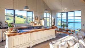 A spacious kitchen with large windows, a wooden island, and a view of the sea. - Loft & Workroom, Woodside Bay | Be My Guest (Auckland)