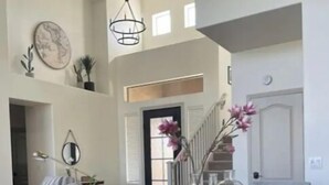 Uma área de refeições com uma mesa de madeira, cadeiras pretas e um vaso com flores cor-de-rosa.
