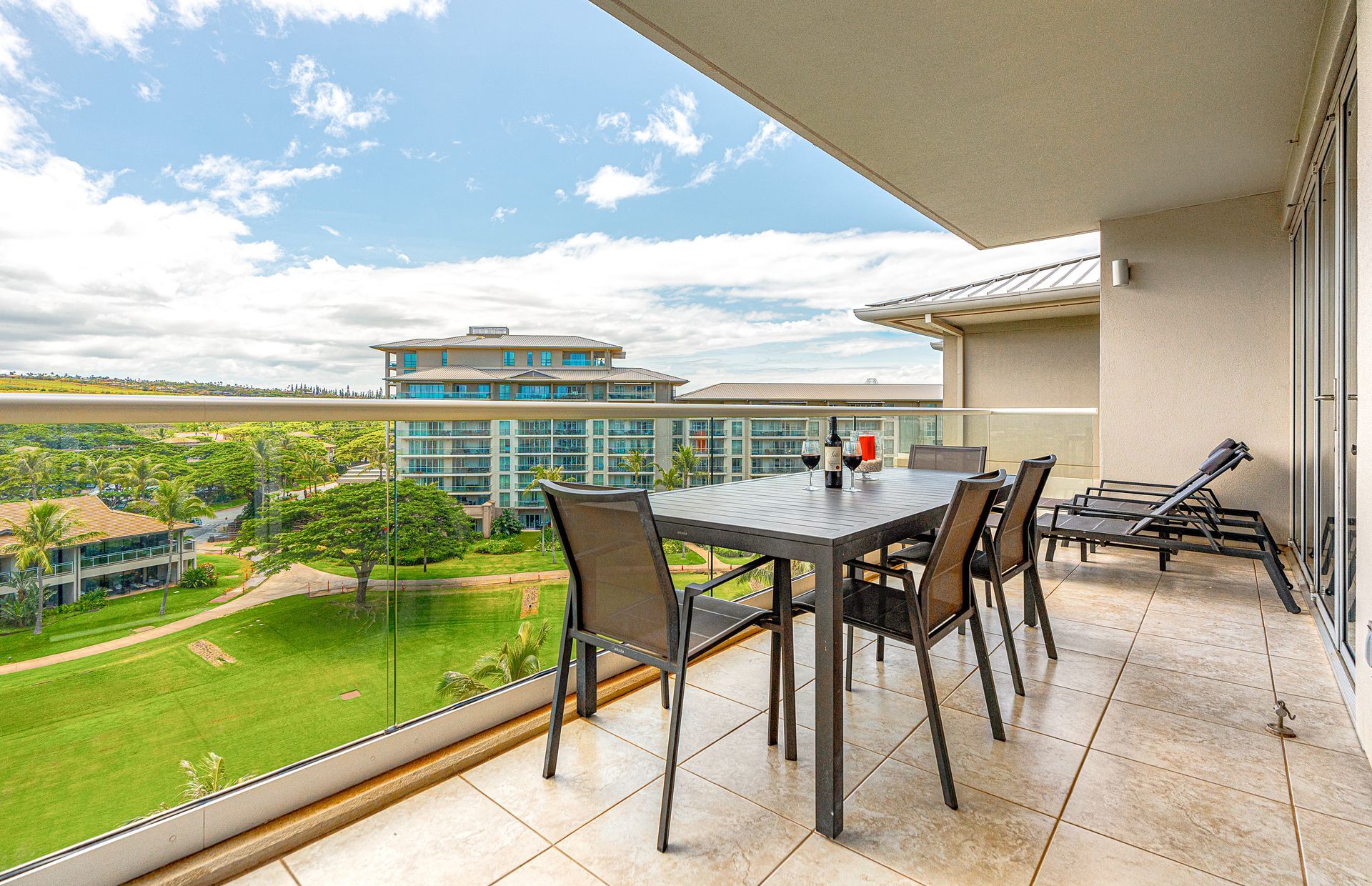 Varanda com mesa e cadeiras, com vista para um edifício e uma paisagem verde.