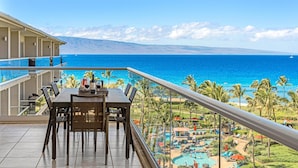 A balcony with a table set for two, overlooking a pool area and the ocean. - Maui Resort Rentals: Honua Kai - 4 Total Bedrooms, 7th Floor Deluxe Ocean AND West Maui Mountain Views (Lahaina)