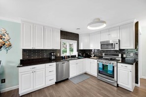 Eine moderne Küche mit weißen Schränken, schwarzen Arbeitsplatten, einem Edelstahl-Geschirrspüler, einem Kombi-Backofen und einer Mikrowelle.
