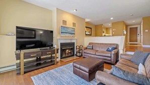 A living room with a flat-screen TV, leather sofas, a fireplace, and a dining area in the background. - Samoset Lakeview Gem - Vibrant Condo Escape! (Gilford)