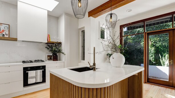 A modern kitchen with a central island, wooden paneling, and a large window offering a view of greenery. - Luna Residence close to Sydney Harbor (North Sydney)