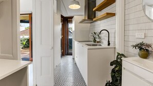 A narrow hallway with a patterned floor, a kitchen area with a sink and a hanging light fixture, and a view into another room. - Luna Residence close to Sydney Harbor (North Sydney)