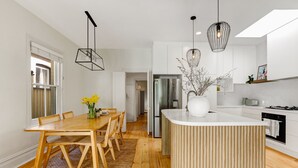 A modern kitchen with a central island, stainless steel appliances, and a dining area with a wooden table and chairs. - Luna Residence close to Sydney Harbor (North Sydney)