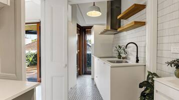 A narrow hallway with a patterned floor, a kitchen area with a sink and a hanging light fixture, and a view into another room.
