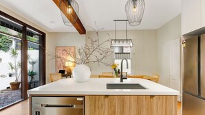 A modern kitchen with a large island, stainless steel appliances, and a view of the garden through the glass door. - Luna Residence close to Sydney Harbor (North Sydney)