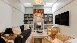 A modern living room with a black sofa, a white coffee table, and wicker chairs. There is a large painting on the wall and a flat-screen TV mounted on the wall. - Luna Residence close to Sydney Harbor (North Sydney)